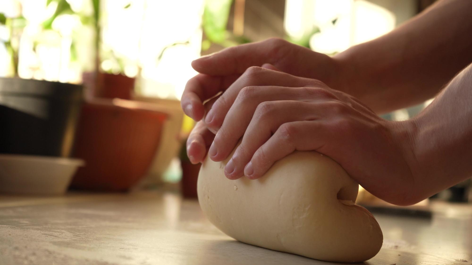 Close-up of hands kneading dough in warm kitchen