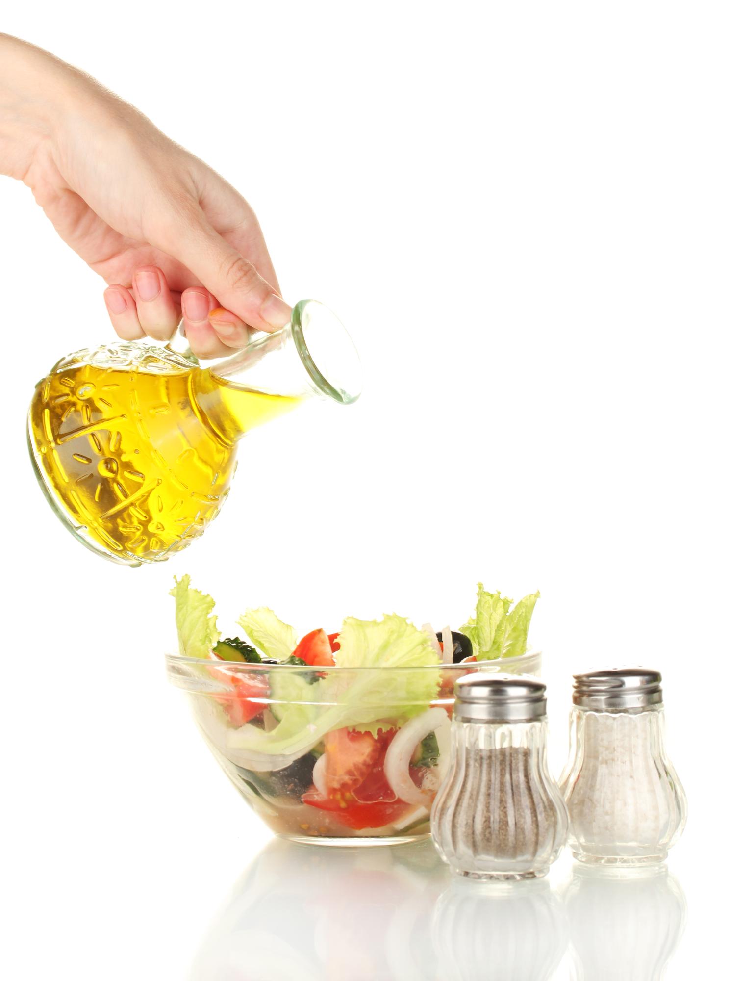 Hand pouring olive oil over salad